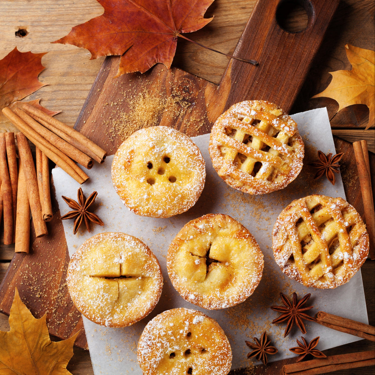 Small baked pastries dusted with cinnamon are arranged with cinnamon sticks and autumn leaves, showing Organic Ceylon Cinnamon Powder used in sweet baking.