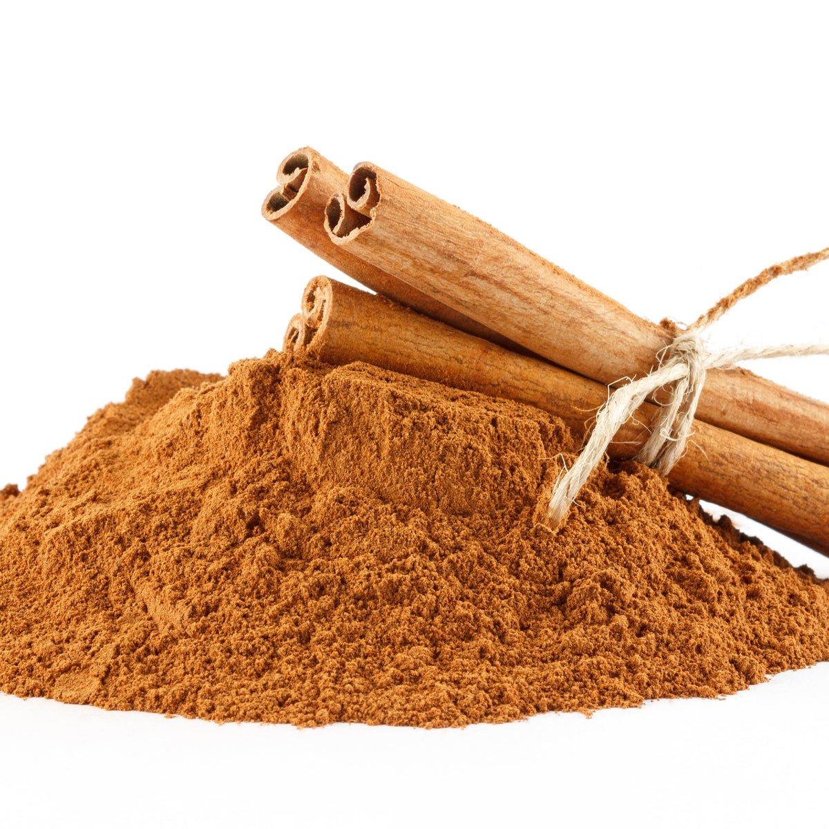A mound of ground Ceylon cinnamon sits beside whole cinnamon sticks against a white background, showing the powdered spice alongside cinnamon bark.