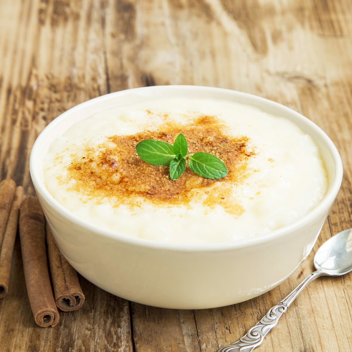 A bowl of creamy rice pudding topped with a dusting of cinnamon and fresh mint, showing Organic Ceylon Cinnamon Powder used as a finishing spice on dessert.