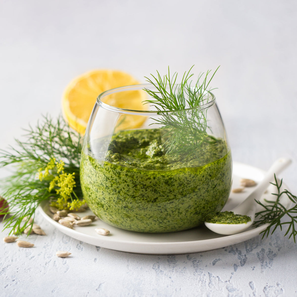 A green herb dressing made with dill is served in a glass bowl and garnished with fresh dill and a slice of lemon.
