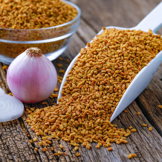 Organic Fenugreek from The Herb Shed Wollongong, Australia, shown as golden-brown seeds spilling from a metal scoop beside a red onion.