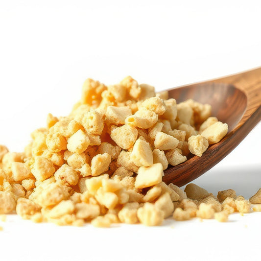 Organic garlic granules spill from a wooden scoop against a white background, showing their coarse chopped texture and natural pale golden colour.