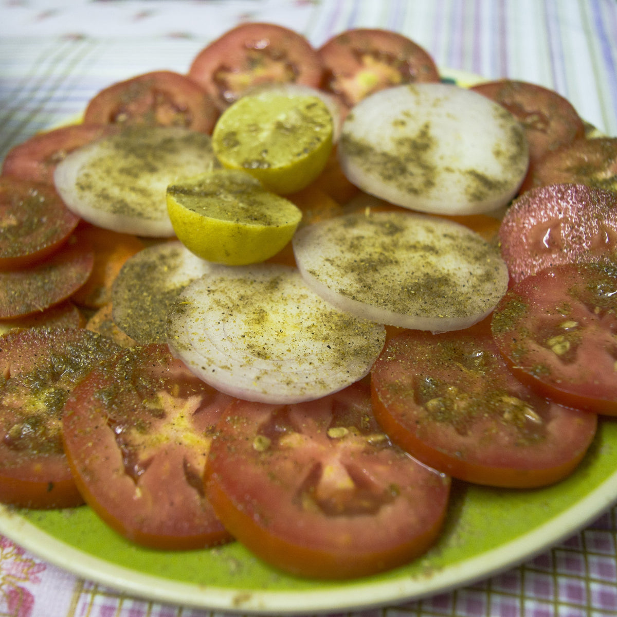 Sliced tomatoes and cucumber are sprinkled with ground coriander and herbs, showing Organic Ground Coriander Seed used to season a fresh savoury salad.