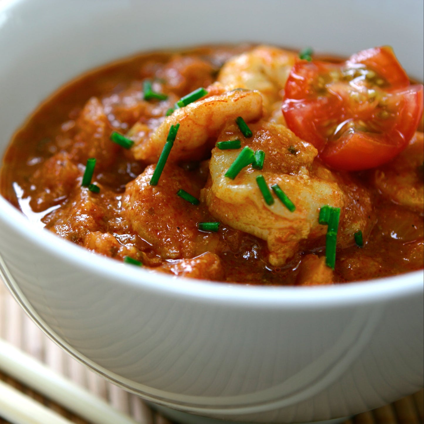 A rich tomato-based cooked dish seasoned with hot paprika is served in a white bowl and finished with fresh green herbs.