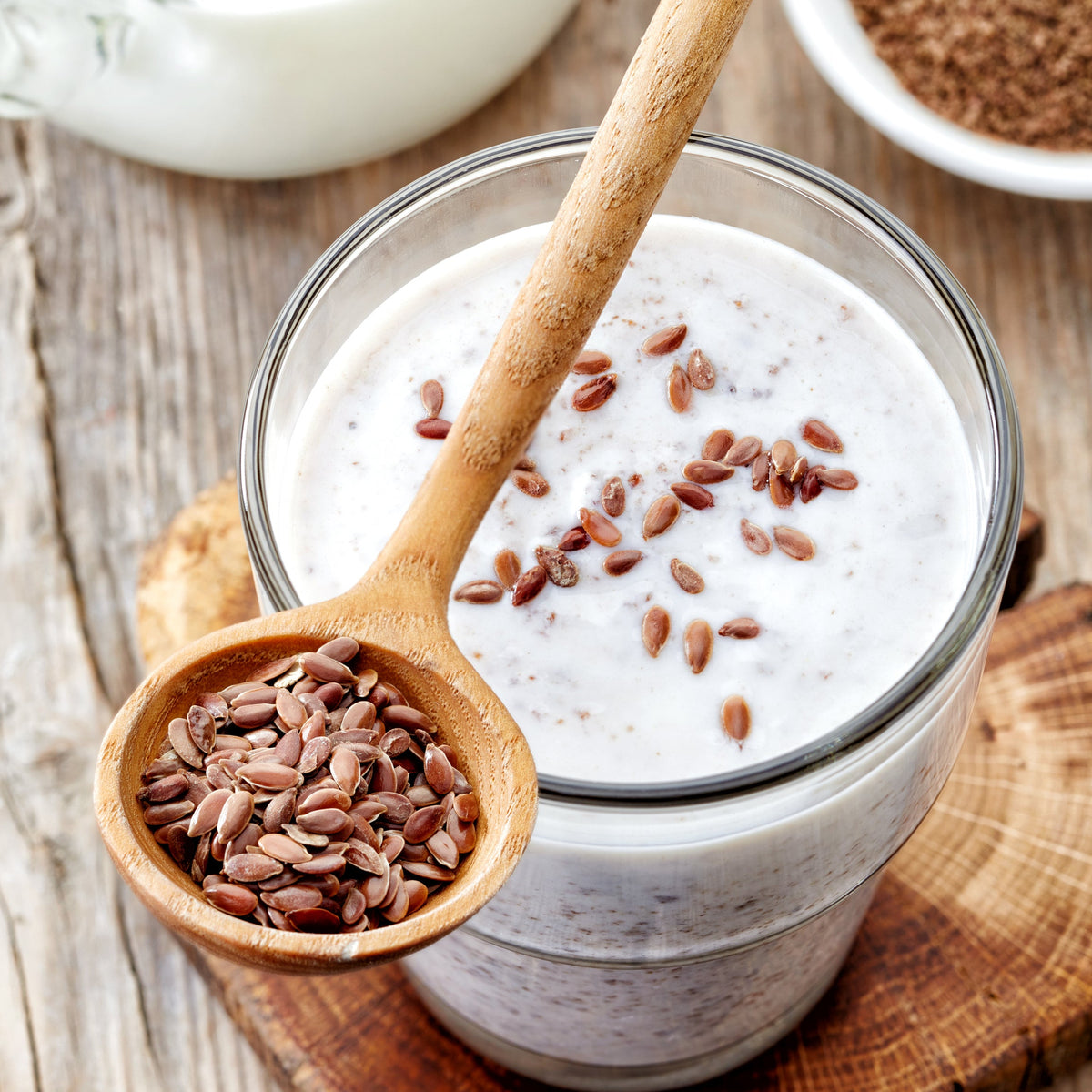 Organic linseeds are sprinkled over a creamy breakfast bowl with additional linseeds in a wooden spoon, showing a simple serving use for The Herb Shed Organic Linseed.