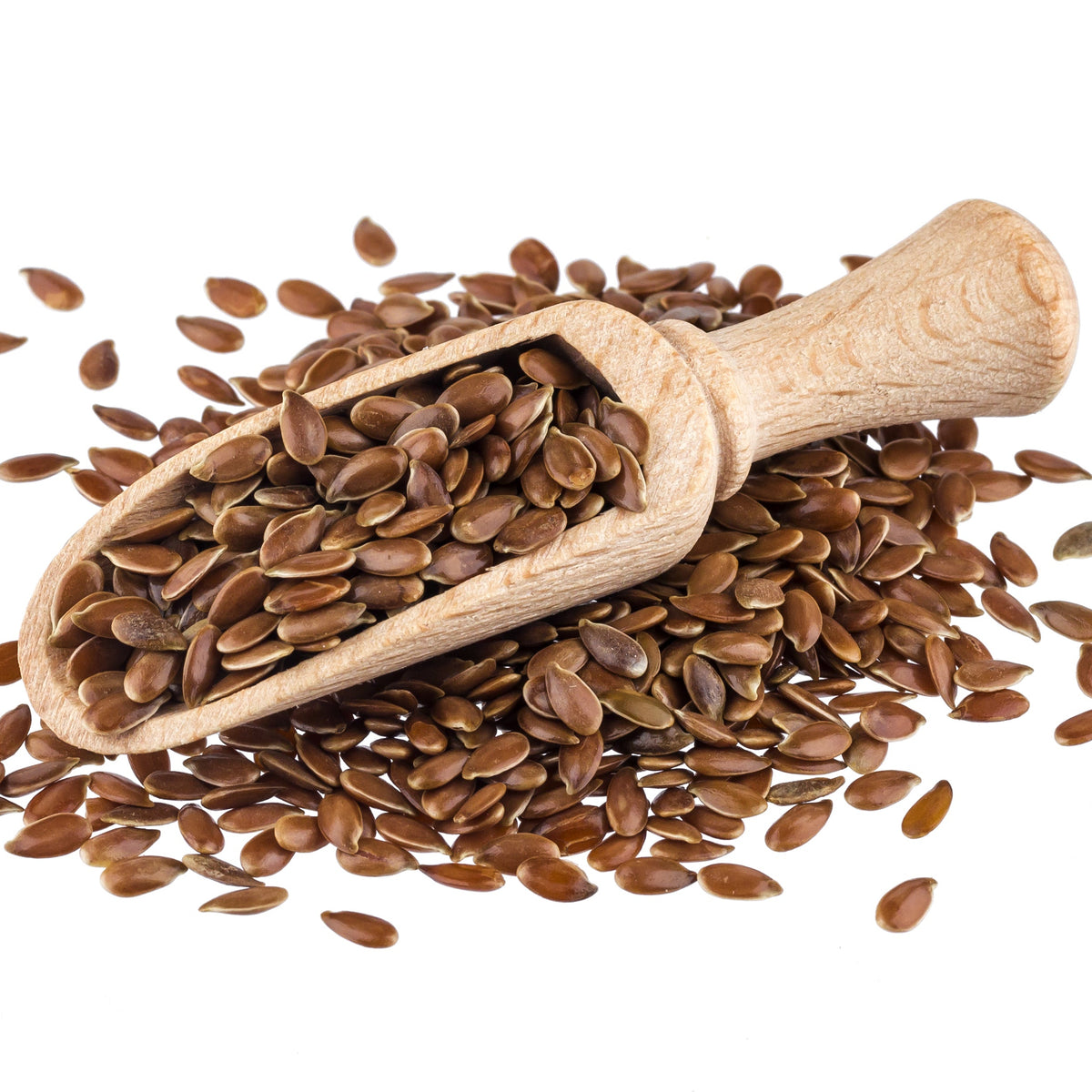 Organic brown linseeds spill from a wooden scoop onto a white surface, showing their small oval shape, smooth texture and glossy brown colouring.