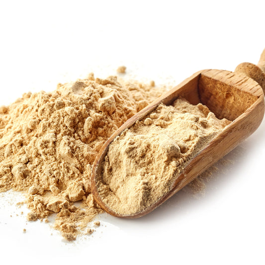 Organic maca powder is piled beside a wooden scoop filled with powder, showing its fine texture and natural pale beige colour.