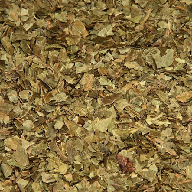 A close-up of organic dried neem leaves showing their cut, coarse leafy texture and natural muted green and brown colouring.
