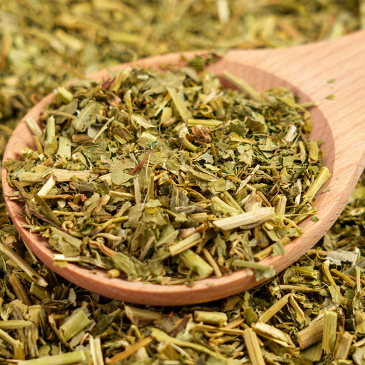 Loose dried organic passionflower sits in a wooden bowl surrounded by dried stems and leaves, showing the green and golden tones of the dried herbal tea.
