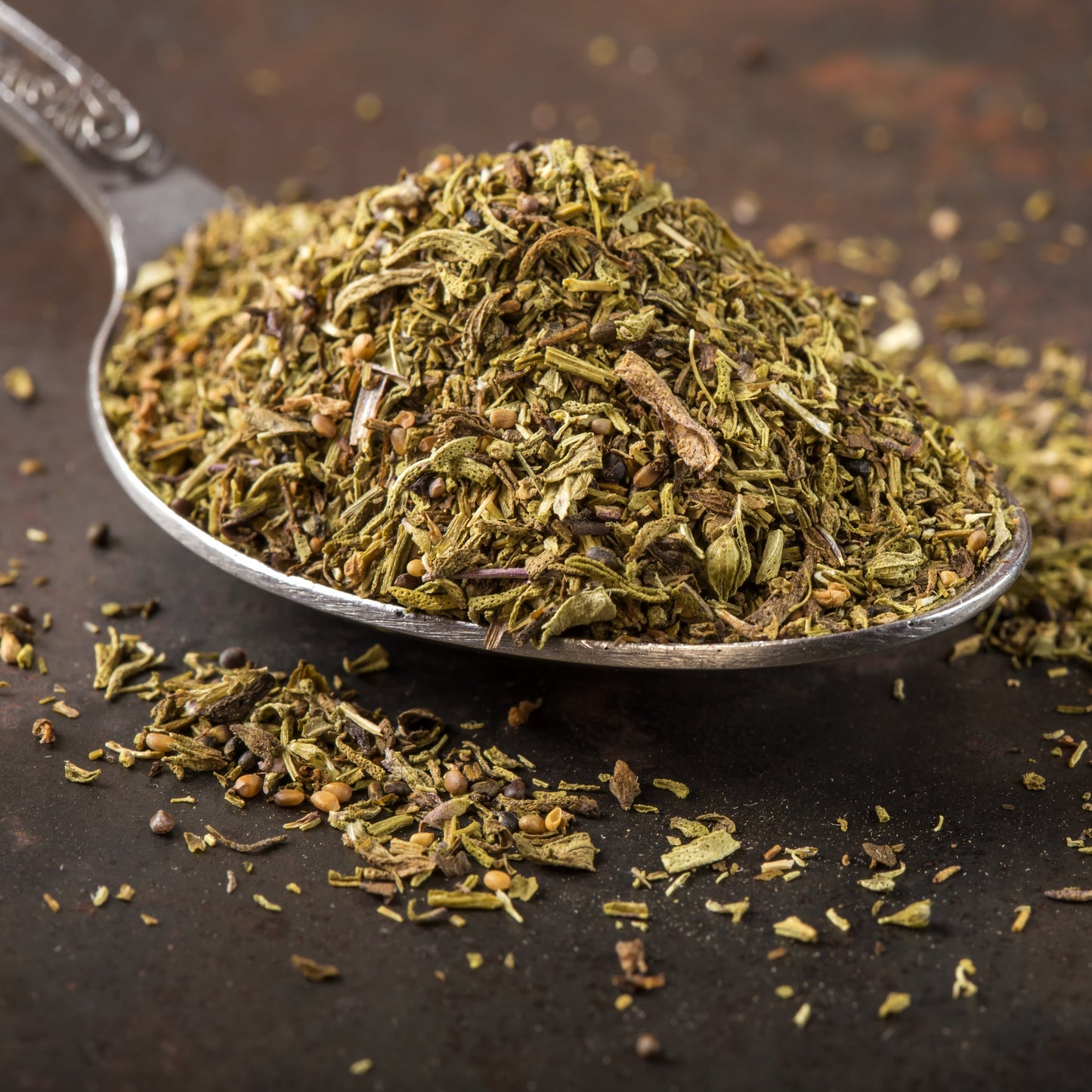 Dried organic thyme fills a metal spoon on a dark rustic surface, with loose thyme scattered around it showing the fine green and brown texture of the dried herb.