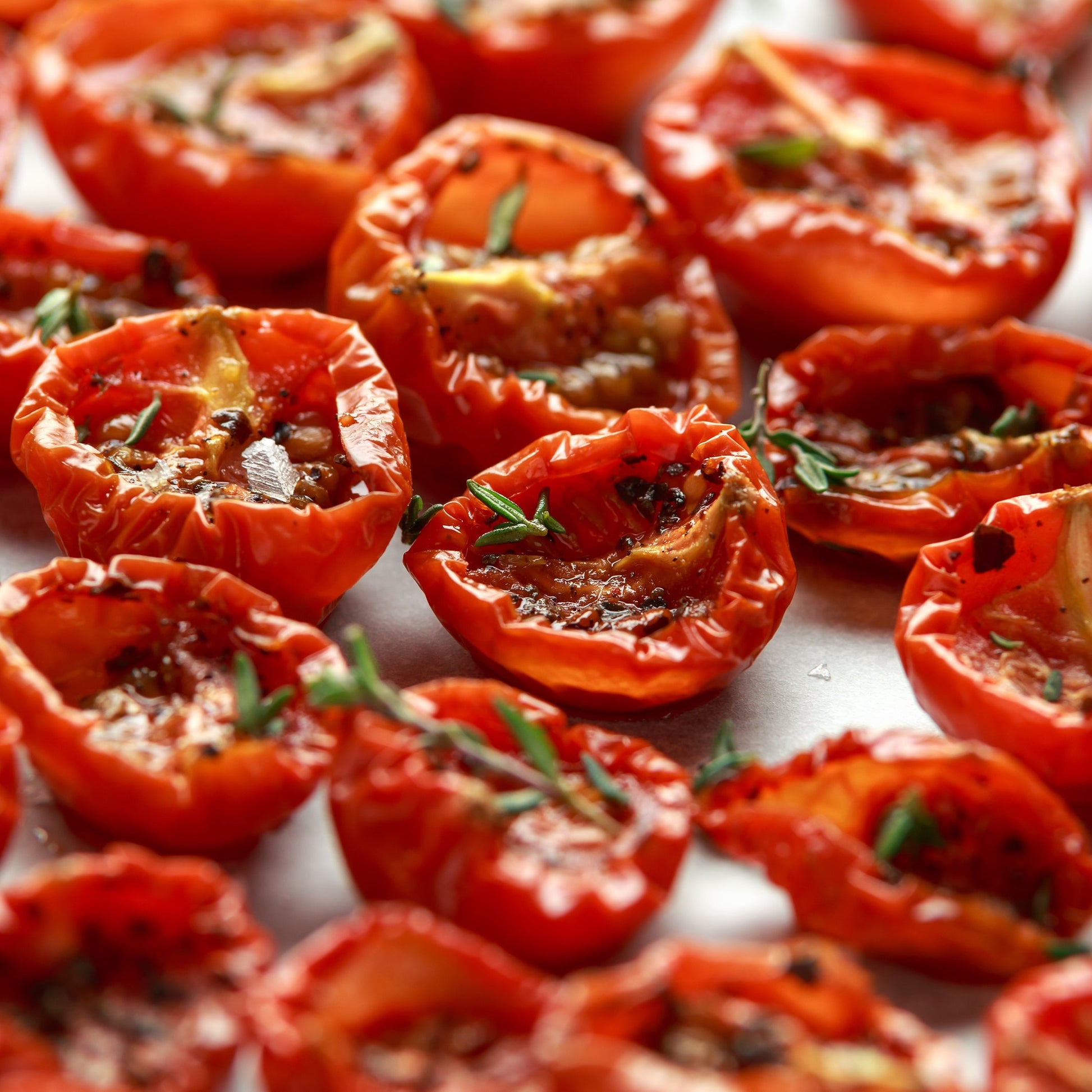 Roasted red tomato halves are seasoned with dried thyme and arranged closely together, showing a savoury serving idea for The Herb Shed Organic Thyme.