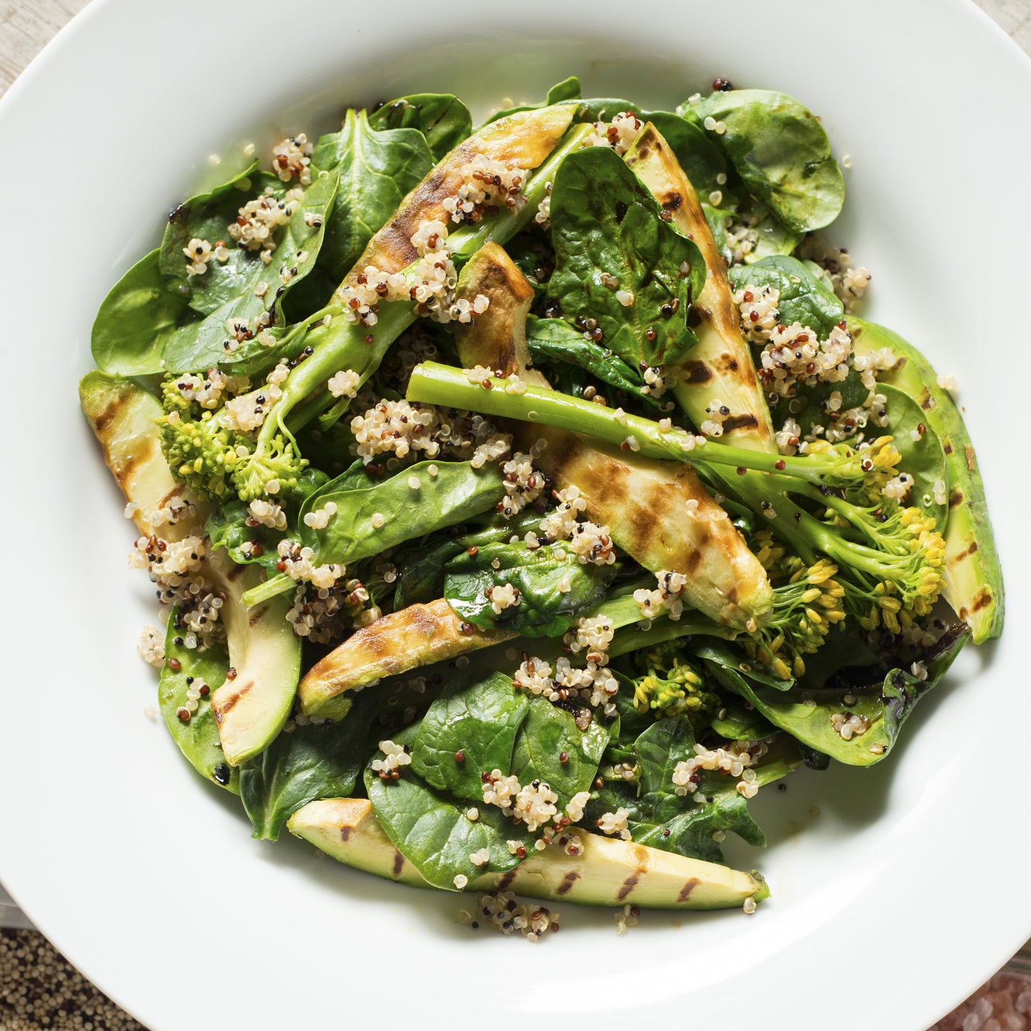 A fresh salad made with organic tri colour quinoa is served with green vegetables and sliced avocado on a white plate.