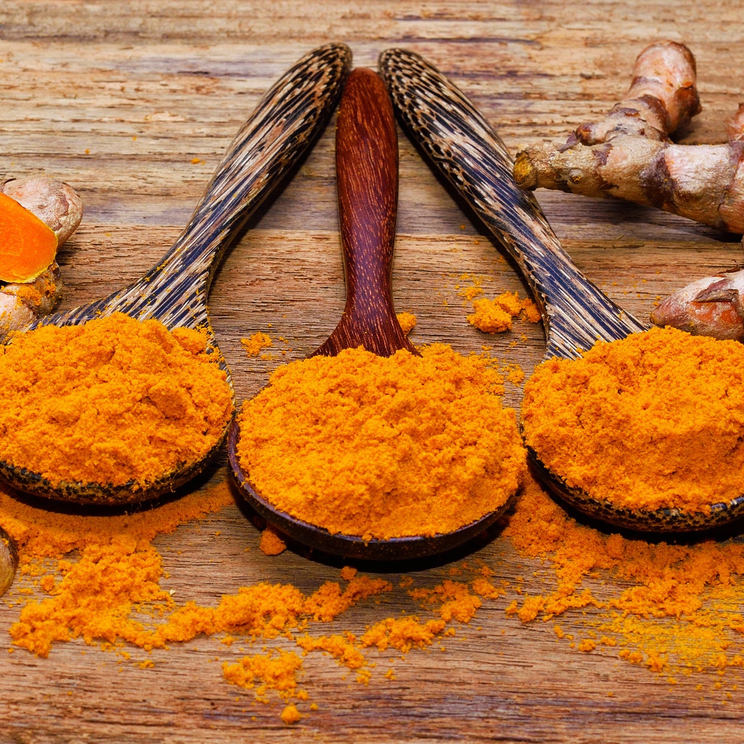 Organic turmeric powder in wooden spoons with whole turmeric