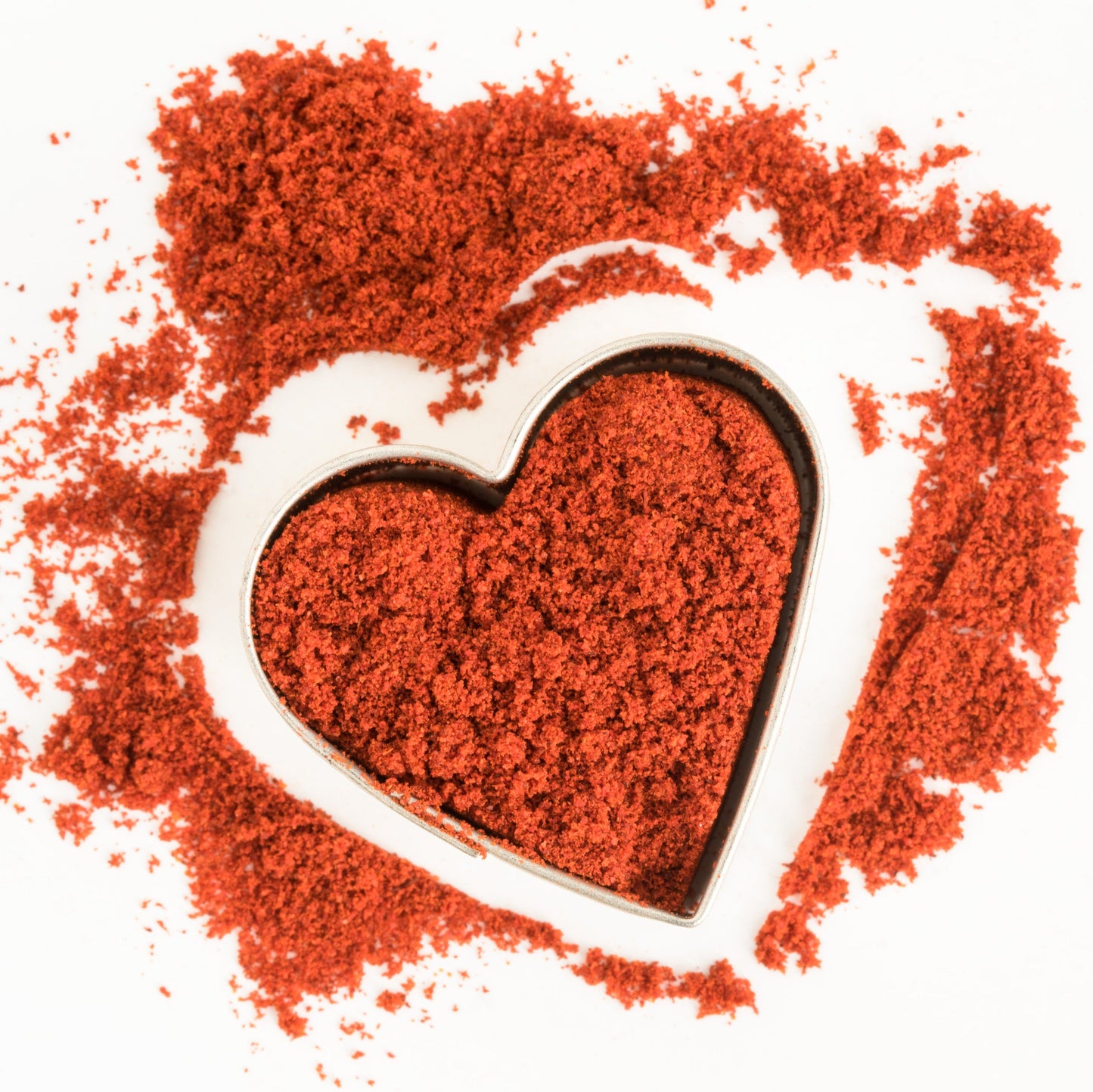Deep red smoked paprika powder is arranged around a heart shape on a white background, showing the rich colour and fine texture of the spice.
