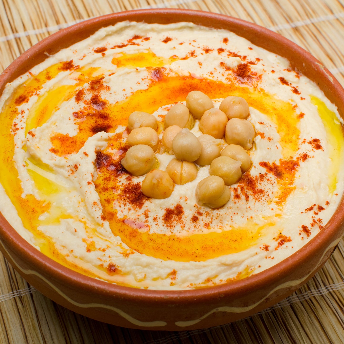 Creamy hummus topped with chickpeas, olive oil and a generous sprinkling of sweet paprika is served in a round bowl.