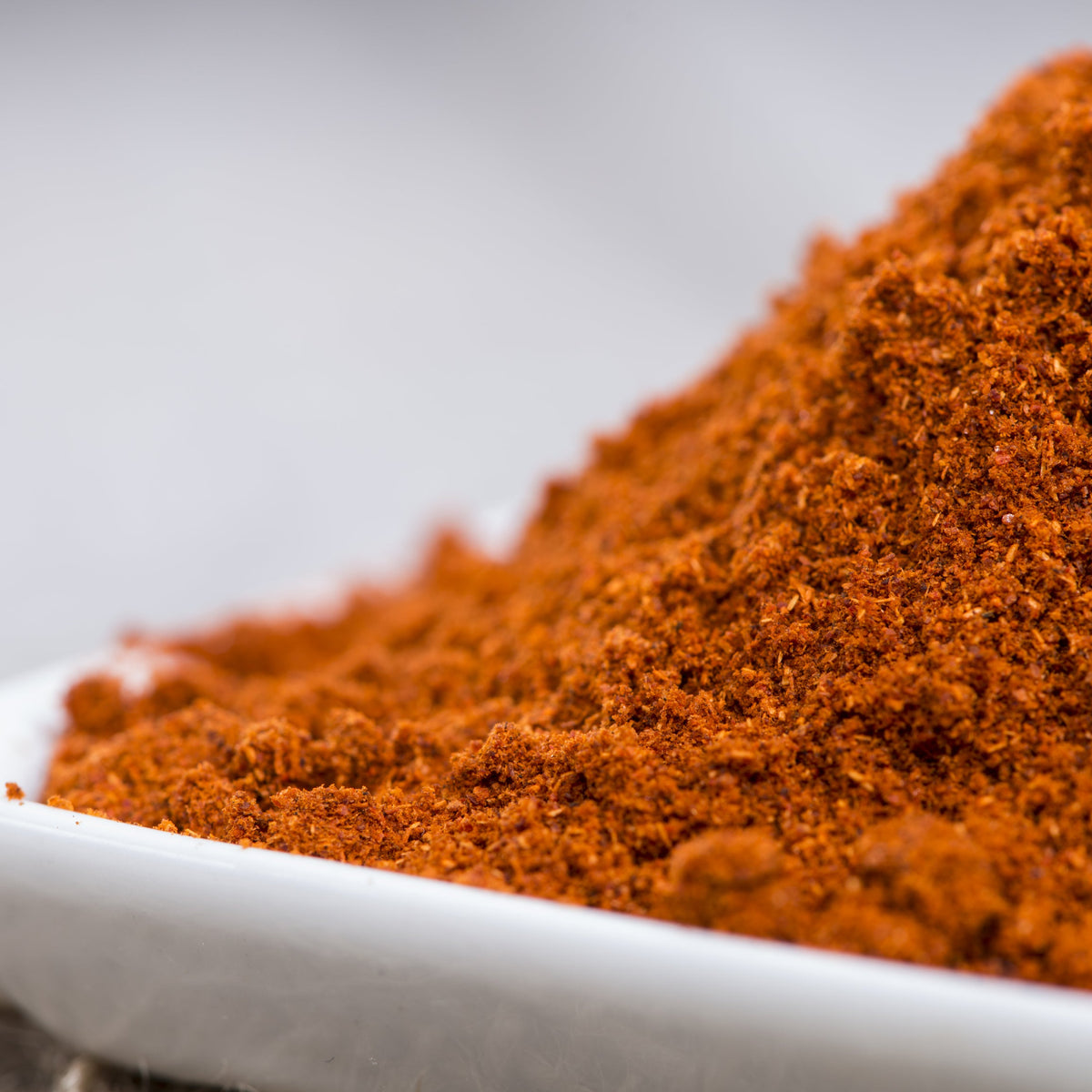 A close-up of finely ground sweet paprika powder piled in a white dish, showing its fine texture and rich red-orange colour.