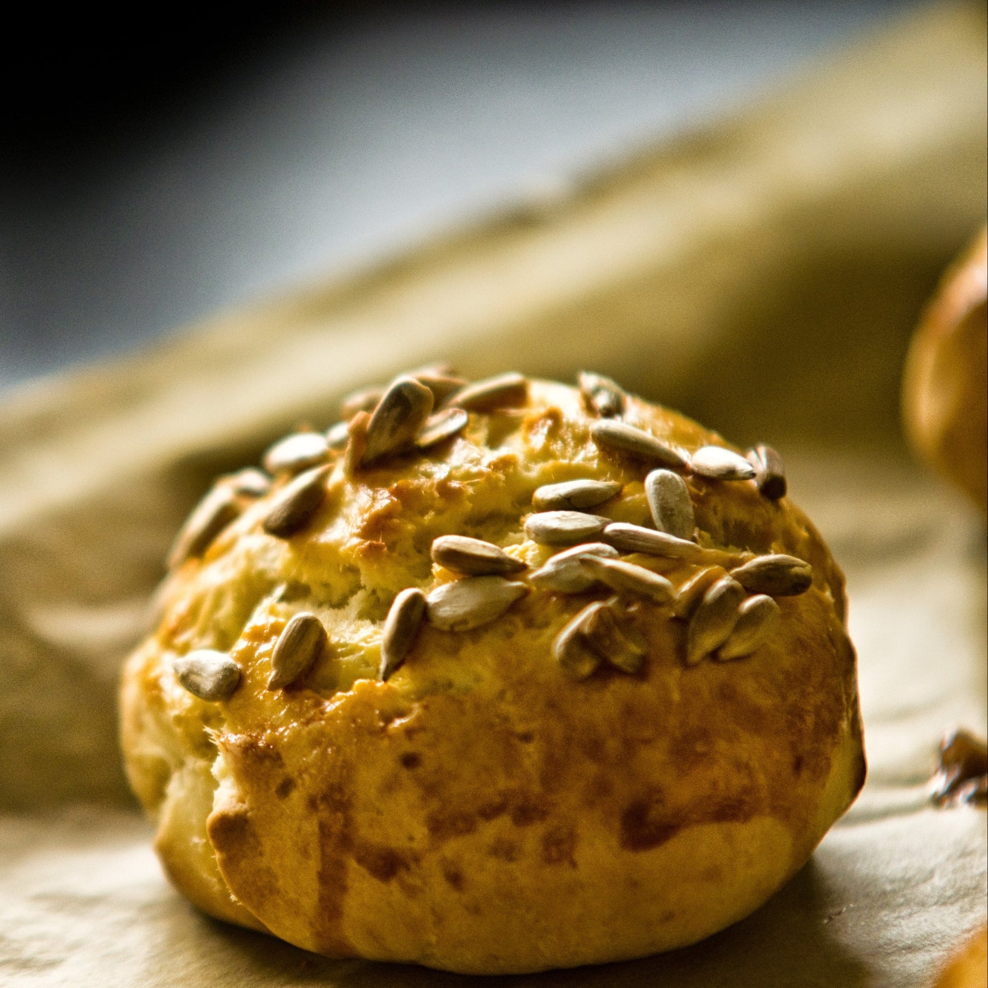 A golden baked muffin topped with sunflower seeds sits on a light surface, showing a baking idea using The Herb Shed Sunflower Seeds.