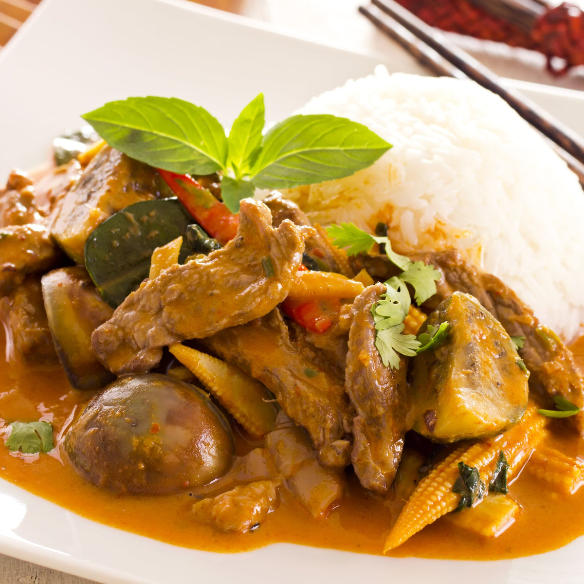 A Thai-style curry with pieces of meat, vegetables and fresh basil in a rich orange sauce, served alongside steamed Thai Jasmine Rice, from The Herb Shed Wollongong Australia.