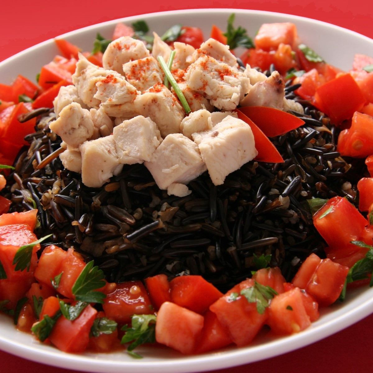 A colourful wild rice salad is served with diced tomatoes, vegetables and cubes of feta cheese, showing a fresh serving idea using The Herb Shed Wild Rice.