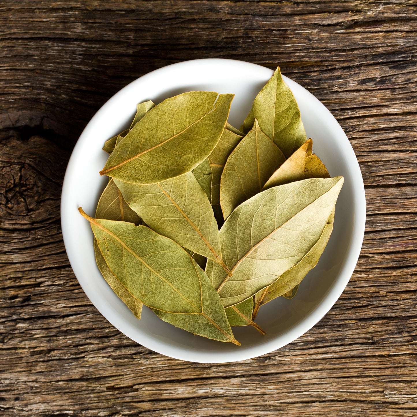 Bay leaves in a white bowl on a wooden table – aromatic green herb from The Herb Shed Wollongong