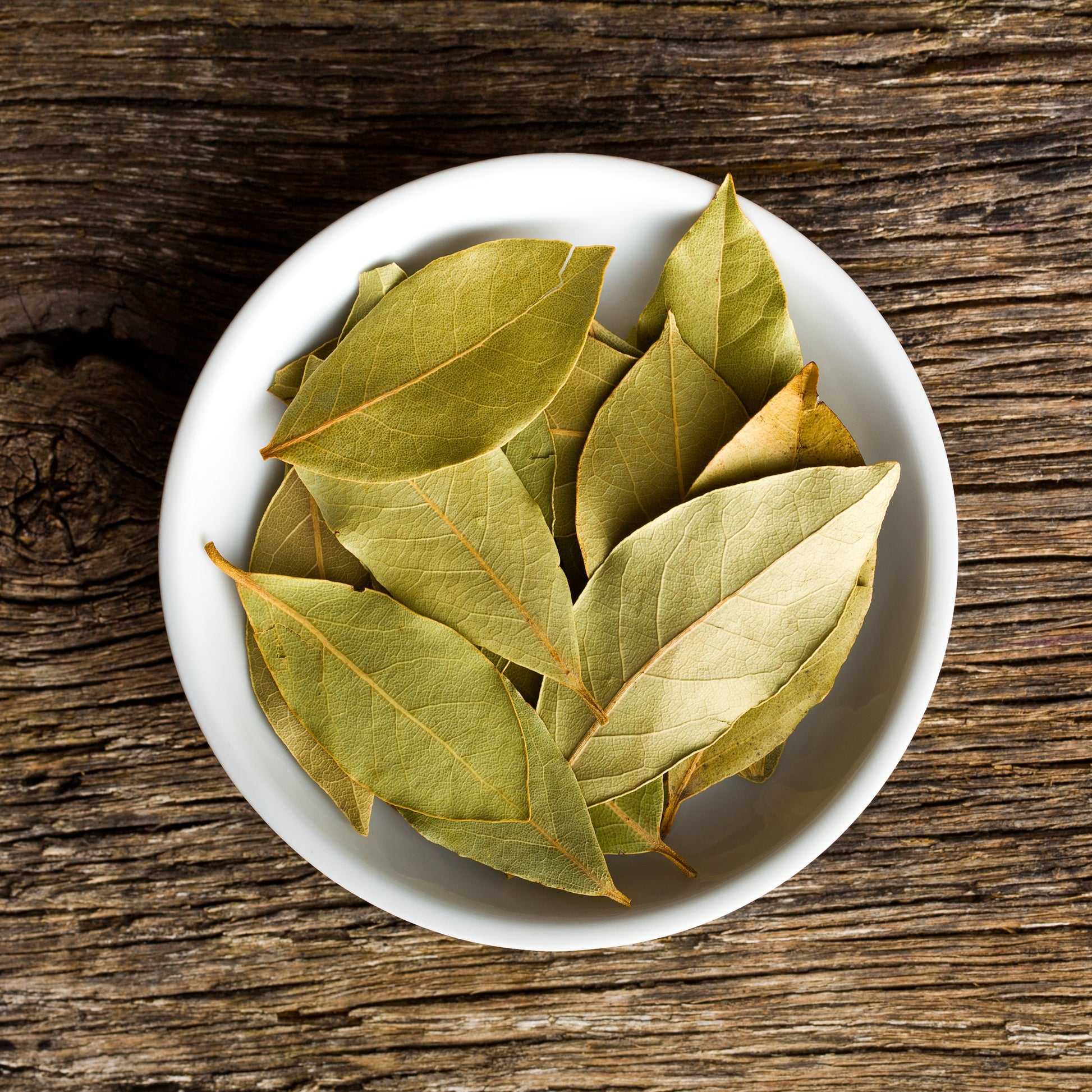 Bay leaves in a white bowl on a wooden table – aromatic green herb from The Herb Shed Wollongong