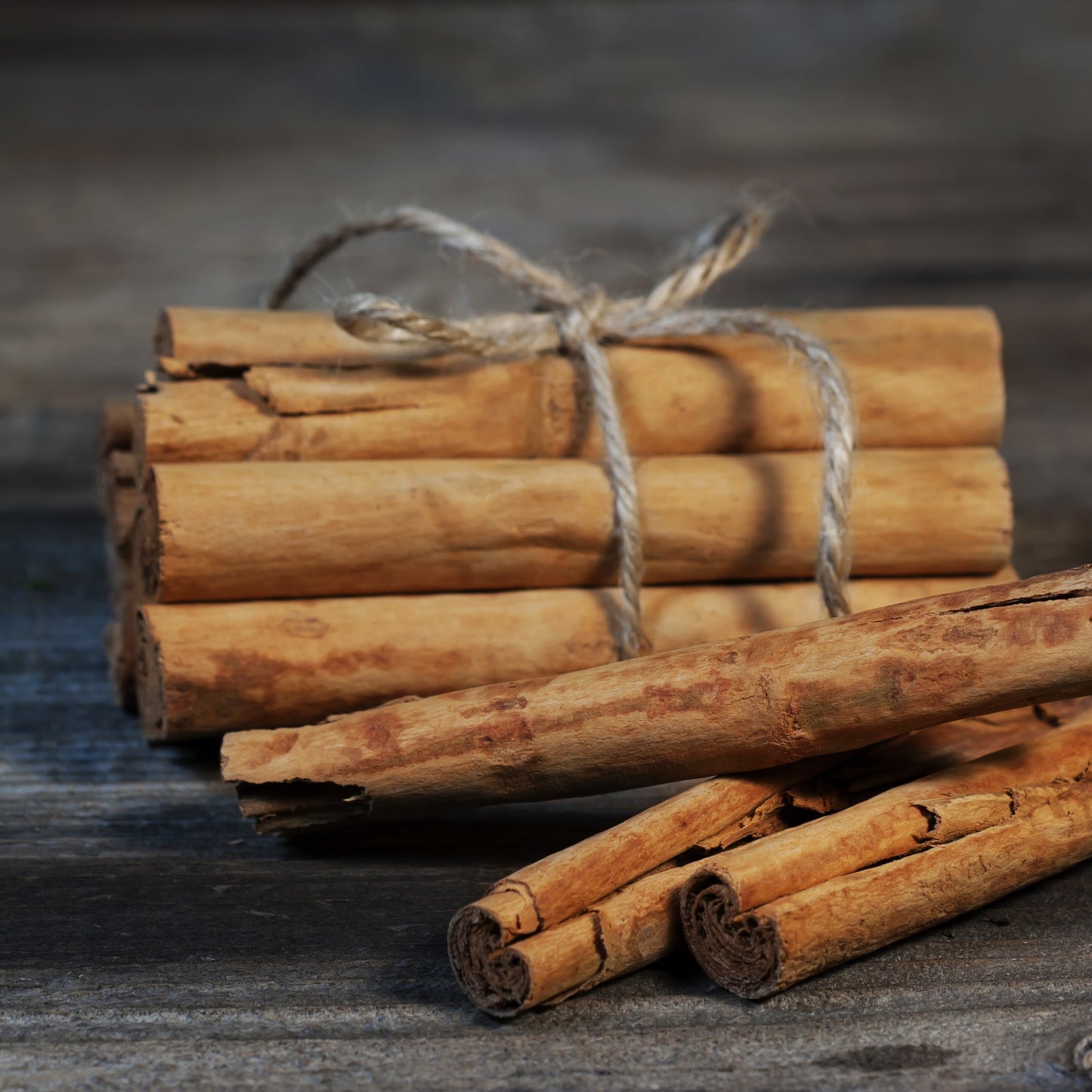 Bundle of natural cinnamon sticks tied with twine on a rustic wooden table, showing warm brown bark texture – The Herb Shed Wollongong