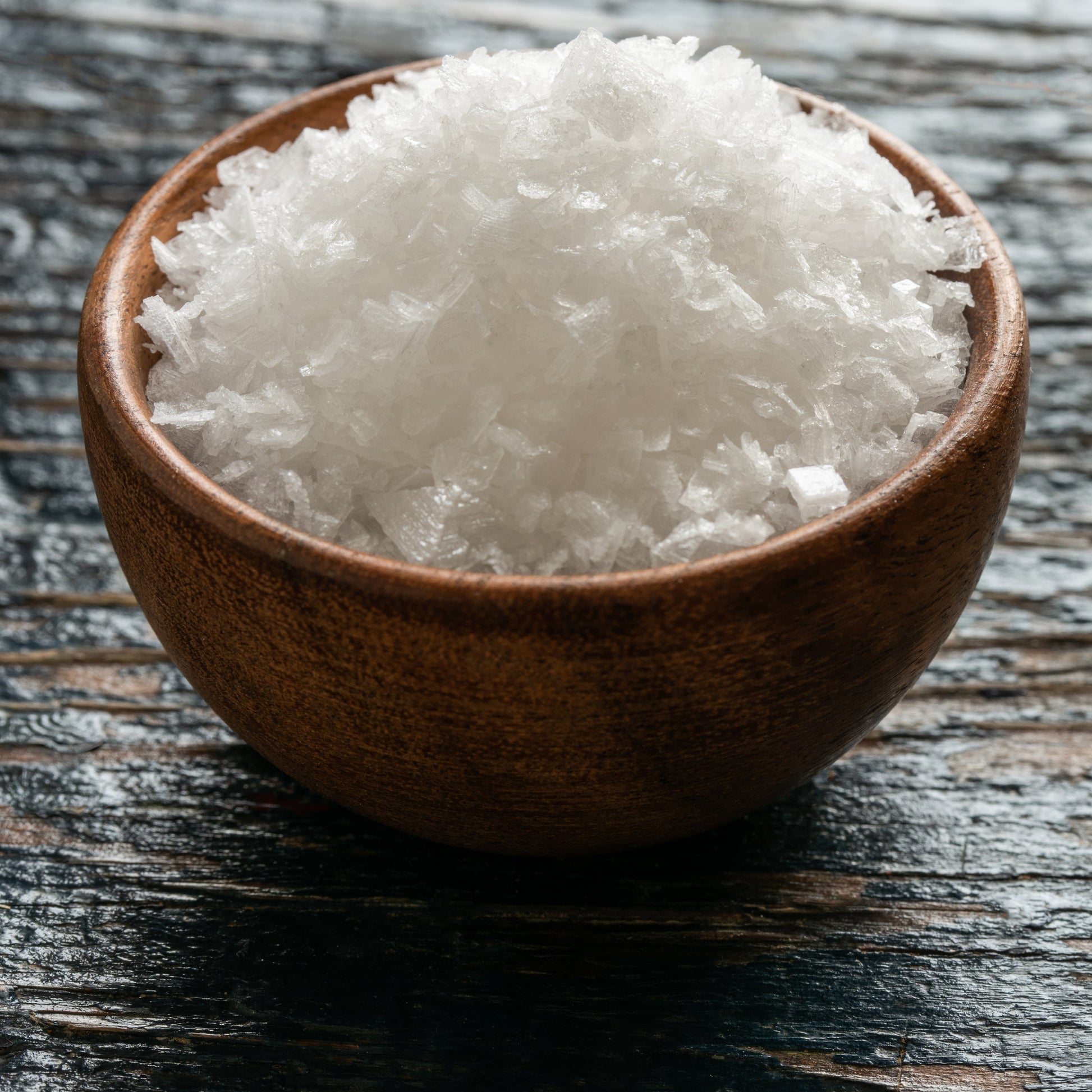 A wooden bowl full of sea salt flakes on a dark wooden table – crisp mineral salt from The Herb Shed Wollongong
