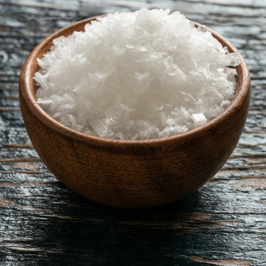 A wooden bowl full of sea salt flakes on a dark wooden table – crisp mineral salt from The Herb Shed Wollongong